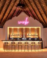 Bar im Nova Maldives Hotel mit leuchtendem Wink-Schild und gefüllten Regalen