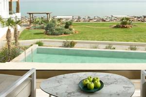 Blick vom Balkon des Mitsis Selection Rinela Hotels auf eine Terrasse mit Tisch, Äpfeln und Blick auf den Pool und das Meer.