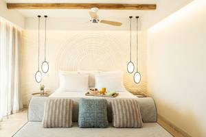 Schlafzimmer im Mitsis Selection Rinela Hotel mit Bett, Tisch, Lampen und Frühstücksplatte