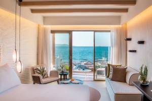 Mitsis Selection Rinela Hotel Zimmer mit Meerblick, modern eingerichtet mit Schlafbereich, Couch, Tisch, Terrasse und Glaswand.