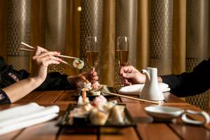 Zwei Personen sitzen an einem Tisch und essen Sushi mit Chopsticks und trinken Champagner.