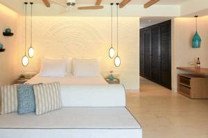 Schlafzimmer im Mitsis Selection Rinela Hotel mit Doppelbett, Couch, Deckenventilator und Wandleuchten.