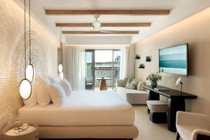 Innenansicht eines Hotelzimmers im Mitsis Selection Rinela mit Bett, Couch, Schreibtisch und Fernseher.