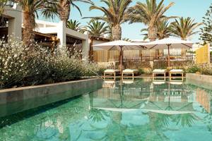 Pool im Mitsis Selection Rinela Hotel mit weißen Sonnenschirmen und Liegen.