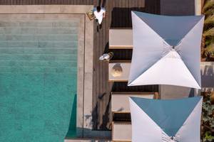 Mitsis Selection Rinela Hotel Außenbereich mit Pool, Sonnenliegen und Sonnenschirmen.