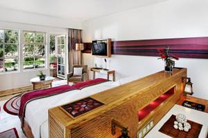 Innenansicht eines Hotelzimmers im Mövenpick Resort & Spa El Gouna mit einem Bett, Fernseher und Pflanzen.