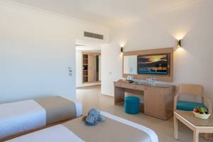 Zimmer im Three Corners Happy Life Beach Resort mit zwei Betten, Schreibtisch, Fernseher und Obstkorb.