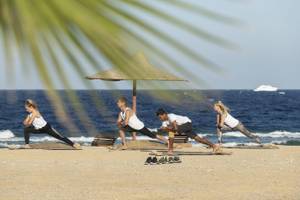 Gruppe von Menschen, die Yoga auf dem Strand unter einem Sonnenschirm machen.