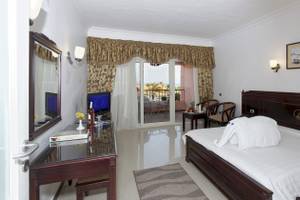 Ein Hotelzimmer im Three Corners Happy Life Beach Resort mit einem Bett, Fernseher, Tisch und einem Balkon.