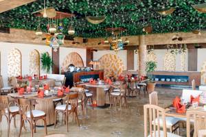 Restaurant im Three Corners Happy Life Beach Resort mit Tisch und Stühlen, geometrischen Wandmustern und dekorativen Lampen.