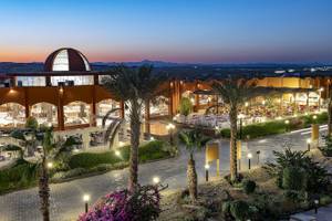 Abendansicht des Three Corners Happy Life Beach Resorts mit beleuchteten Palmen und Gebäuden.