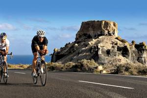 Zwei Radfahrer fahren auf einer Straße mit Felsen im Hintergrund.