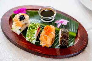 Ein Teller mit verschiedenen Sushi-Variationen auf einem Blatt serviert, mit Sojasauce.