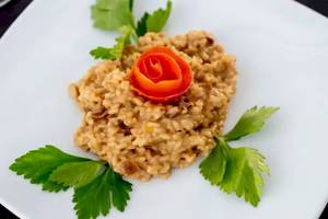 Risotto mit Pilzen und Rose auf einem weißen Teller serviert.