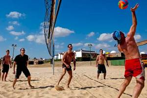Mehrere Männer spielen Volleyball auf einem Sandstrand in der Nähe eines Hotels.