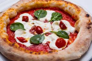 Pizza mit Mozzarella und Spinat auf einem weißen Teller serviert