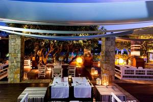 Außenbereich des Elounda Beach Hotel & Villas bei Nacht mit beleuchteten Tischen und Stühlen.
