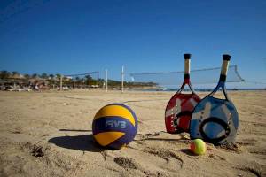 Volleyball-Ausrüstung auf einem sandigen Strand mit einem Volleyball, Tennisschläger und einem Tennisball.