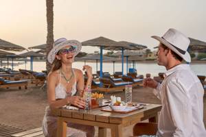 Eine Frau und ein Mann sitzen am Tisch am Strand, essen und trinken