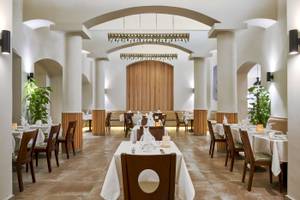 Innenansicht des Restaurants im Three Corners Rihana Resort mit Tisch und Stühlen, weißen Tischdecken, dekorativen Pflanzen und Holzelementen.