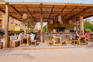 Gäste sitzen an Tischen im Freien unter einem Holzpavillon im Three Corners Rihana Resort.