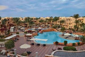 Außenbereich des Steigenberger Coraya Beach Hotels mit Swimmingpool, Liegestühlen und Palmen.
