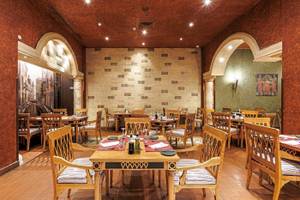 Restaurant im Sunrise Royal Makadi Resort mit Holztischen und Stühlen, gemusterten Wänden und Deckenbeleuchtung.