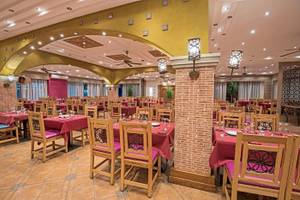Innenbereich des Restaurants des Sunrise Royal Makadi Resort mit gedeckten Tischen, Holzstühlen und gemusterten Kissen.