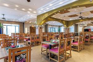 Innenbereich des Restaurants im Sunrise Royal Makadi Resort mit Holztischen und Stühlen, Deckenventilatoren und beleuchteten Decken.