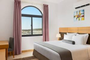 Wyndham Garden Salalah Mirbat Hotel Zimmer mit Bett, Schreibtisch und Fenster mit Meerblick.
