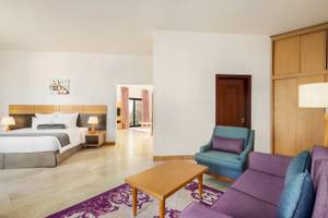 Schlafzimmer im Wyndham Garden Salalah Mirbat Hotel mit Doppelbett, Nachttischen, Lampen, Teppich und Wohnzimmermöbeln.