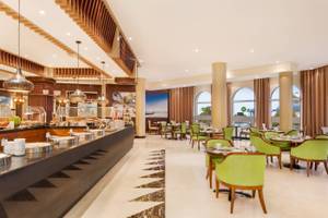 Innenbereich eines Restaurants im Wyndham Garden Salalah Mirbat Hotel mit grünen Stühlen und Tischen.