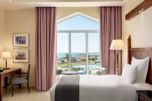 Zimmer im Wyndham Garden Salalah Mirbat Hotel mit Meerblick, großes Bett, Schreibtisch und Panoramafenster.