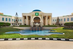 Außenansicht des Wyndham Garden Salalah Mirbat Hotels mit Brunnen und Rasenfläche.