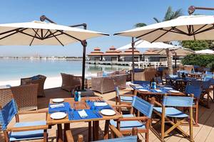 Außenrestaurant am Strand des Anantara The Palm Dubai Resort mit Tischen und Stühlen unter Schirmen.