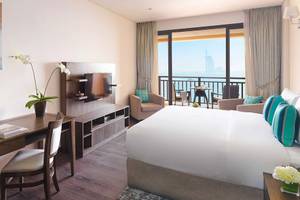 Suite Zimmer im Anantara The Palm Dubai Resort mit Schreibtisch, Lampe, Bett und Meerblick.
