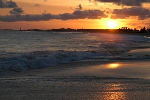 Sonnenuntergang am Strand mit Wellen, die auf den Strand treffen.
