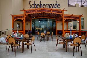 Außenbereich des Scheherazade Hotels mit runden Tischen und Stühlen unter einem hölzernen Baldachin.