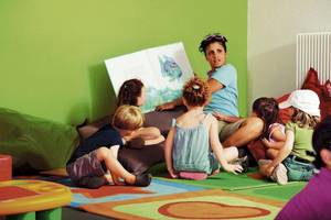 Eine Frau liest Kindern ein Buch vor in einem grün gestrichenen Raum