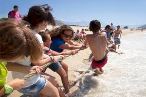 Kinder ziehen einen Jungen am Strand im Wasser an einem Seil