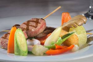 Gegrillter Fleischspieß mit Gemüse auf einem weißen Teller, serviert im Atrium Palace Thalasso Spa Resort & Villas.