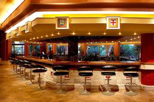Innenansicht der Bar des Atrium Palace Thalasso Spa Resort & Villas mit Barhockern und einer Theke.