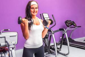 Frau im Fitnessstudio, die Hanteln hält und lächelt