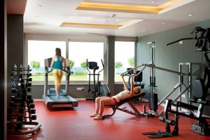 Fitnessraum im Pernera Beach Hotel mit einer Frau auf einer Bankbank und einer anderen Frau auf einem Laufband.