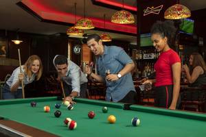 Im Hotel Jumeira Rotana spielen Gäste Billard in einer Bar mit bunten Lichtern und Fernsehern.