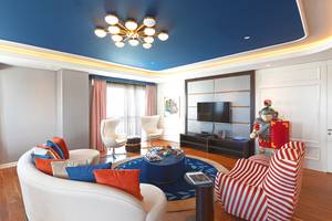 Wohnzimmer im Hotel The Land of Legends Kingdom mit blauer Decke, Kronleuchter, Fernseher, Tisch, Stühle und römischer Statue.