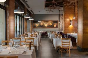 Innenansicht des Rixos Bab Al Bahr Restaurants mit Tisch und Stühlen, Holzwänden und Kronleuchtern.
