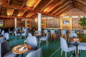 Innenbereich des Grand Sirenis Punta Cana Resort mit mehreren Tischen und Stühlen, Fernsehern an der Wand und einer grünen Spielfläche.