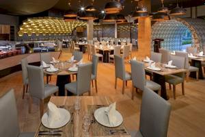Innenansicht des Restaurants im Grand Sirenis Punta Cana Resort mit hölzernen Tischen und Stühlen.