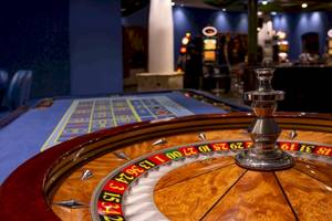 Casino-Spieltisch mit einem großen, auffälligen Roulette-Rad im Vordergrund.